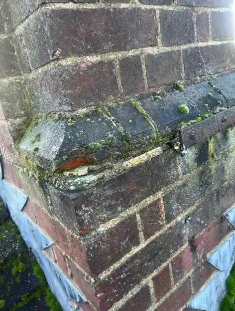 Chimney with a cracked mortar fillet, worn flashing and moss on the brickwork