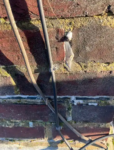 Chimney brickwork with old cables and failed flashing tape at the base