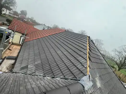 New grey tile re-roof meeting a neighbouring red tile roof, scaffold in place