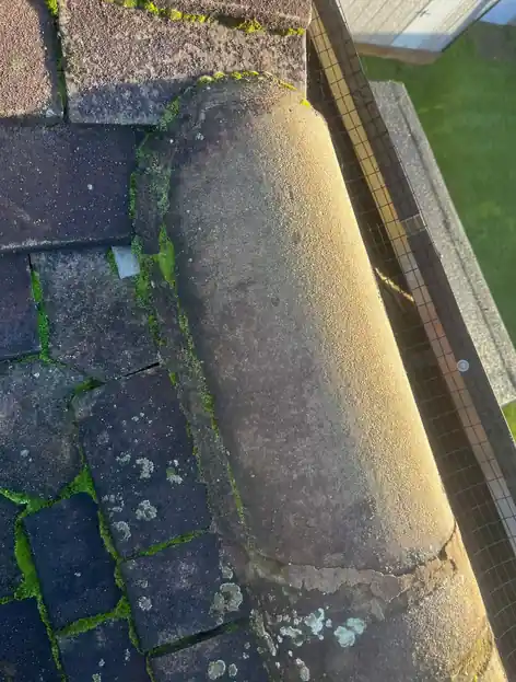 Half-round ridge tile with cracked mortar and moss on the tiles below