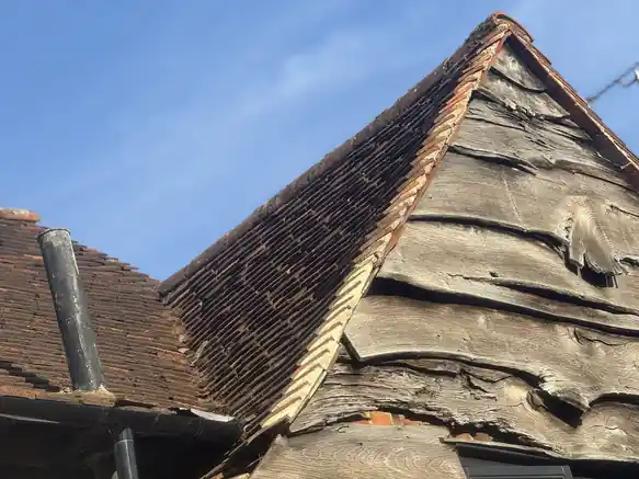 Old plain tile roof with perished felt hanging out at the gable
