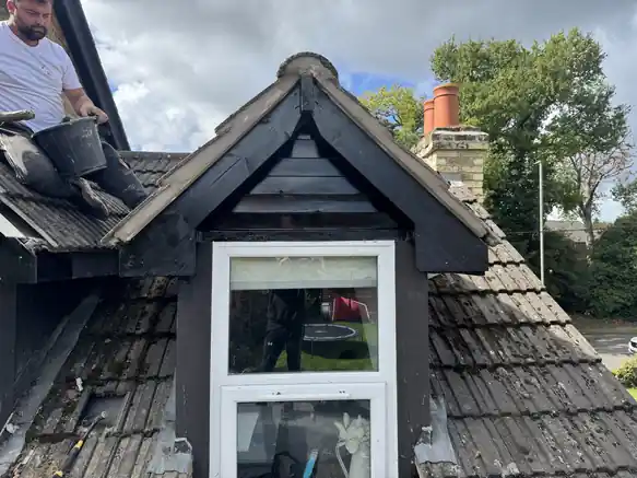 Roofer working beside a black-clad dormer on a concrete tile roof