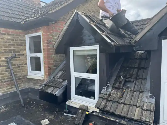 Roofer rebuilding a black-clad dormer with the tiles stripped back around it