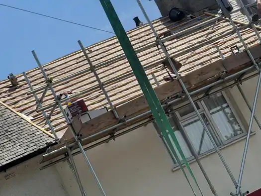 Scaffold round a house with the old roof stripped back to the battens