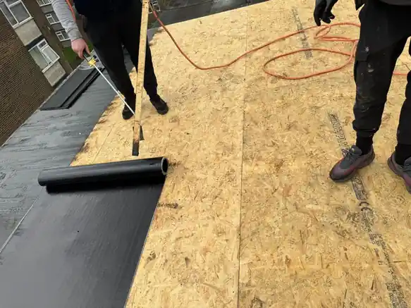Roofers rolling out underlay over a new OSB flat roof deck